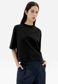 Schwarzes Baumwoll-T-Shirt mit Rundhalsausschnitt und kurzen Ärmeln, im lässigen Schnitt und mit glatter Textur, kombiniert mit marineblauen hochtaillierten Hosen.