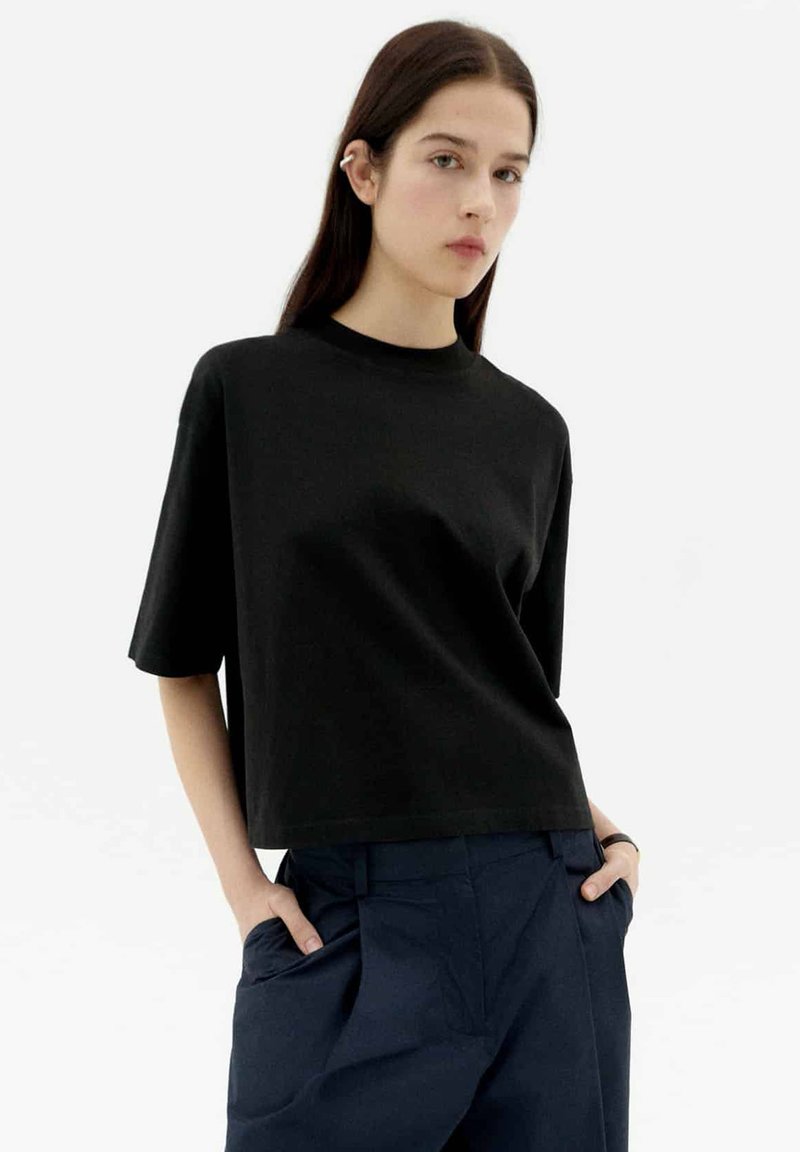 Schwarzes Baumwoll-T-Shirt mit Rundhalsausschnitt und kurzen Ärmeln, im lässigen Schnitt und mit glatter Textur, kombiniert mit marineblauen hochtaillierten Hosen.