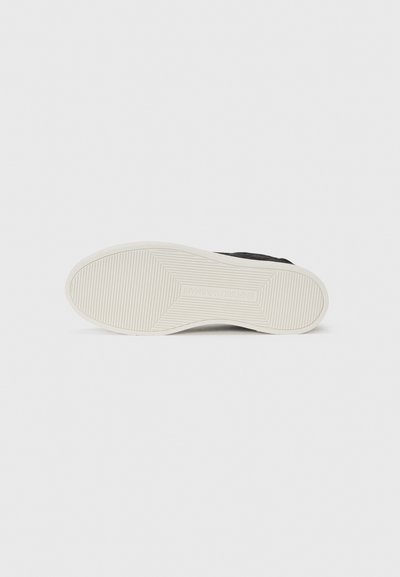 Semelle de sneaker noire avec une surface texturée et à motifs. Caoutchouc de couleur crème avec des rainures pour l'adhérence. Design simple et minimaliste sans branding visible.