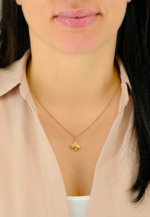 Collana d'oro con un pendente testurizzato a forma di testa di animale stilizzata, indossata sopra una blusa di un rosa chiaro. La catena è sottile e delicata.