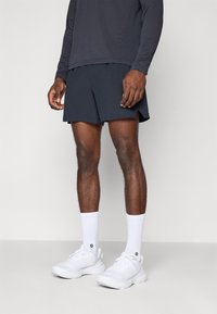 Athletic outfit featuring a long-sleeve dark top, dark shorts with side slits, white socks, and white athletic shoes with textured uppers.