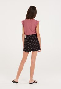 Roze geribbelde top met ruches aan de mouwen, gecombineerd met zwarte patroonshorts met een rood diamanten ontwerp, gedragen met zwarte flip-flops.