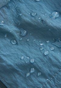 Vattentåligt tyg i blått med droppar på ytan; slät textur med synliga sömmar och en lätt lyster.