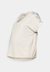 Světlé béžové těhotenské tričko s výstřihem do V, krátkými rukávy a krajkovými detaily na ramenou. Měkká, elastická látka s volným střihem.