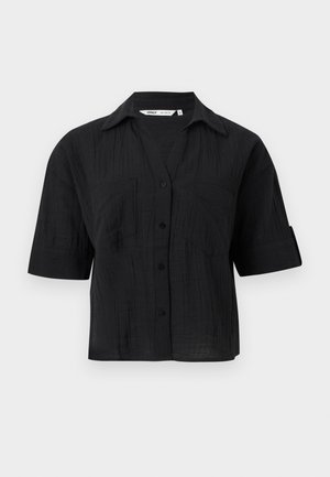 Črna srajca s kratkimi rokavi na gumbke z ovratnikom, teksturirano tkanino, dvema prsnikoma in zavihki na rokavih na svetlo sivi podlagi.
