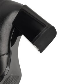 Chaussure à talons hauts noire avec une finition brillante, un talon épais et texturé, et une semelle texturée, avec des coutures visibles le long du dessus.