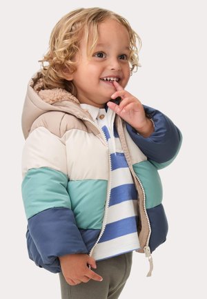 Gepolsterte Jacke mit Kapuze. Farben: beige, türkis, blau. Verfügt über ein weiches Futter, einen Reißverschluss und ein Color-Block-Design. Getragen mit einem gestreiften Shirt.