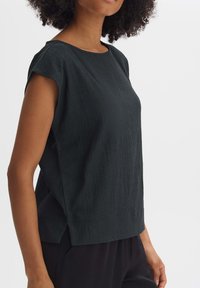 Top corto verde scuro a maniche corte con un tessuto testurizzato, scollatura rotonda e fessure laterali, completato da una vestibilità rilassata e un design semplice.