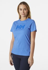 Camiseta corta de manga azul hecha de algodón, con un prominente logo azul "HH" y el texto "HELly HANSEN" en la parte frontal. Textura suave.