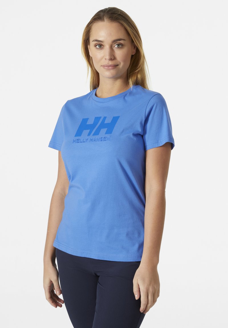 Camiseta corta de manga azul hecha de algodón, con un prominente logo azul "HH" y el texto "HELly HANSEN" en la parte frontal. Textura suave.