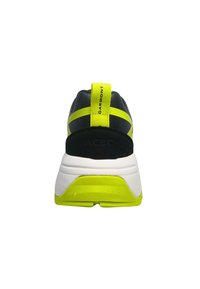 Scarpe da ginnastica nere e gialle con tomaia testurizzata, dettagli gialli vivaci e intersuola bianca, dotate di un caratteristico tassello sul tallone.