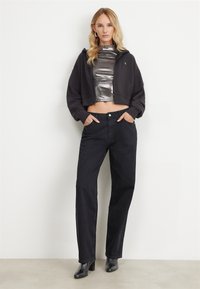 Un sweat à capuche noir largement coupé sur un haut métallisé argent à col montant, associé à un jean noir taille haute et des bottines noires à talons.