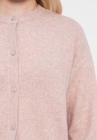 Rosa kofta i mjukt stickat tyg, med rund hals, långa ärmar och fem matchande knappar fram.