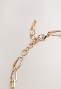 Gold metal chain with large, interlocking links and a clasp. Features a small tag attached. Smooth texture with a shiny finish.