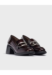 Mocasines de charol burdeos con un acento en hardware de tono plateado y un tacón negro grueso, con una superficie lisa y pulida.