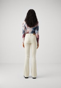 Tricou cu mânecă lungă, vopsit în nuanțe pastelate, cu un design ajustat; asortat cu pantaloni flared de culoare fildeş şi încălţămite negre.