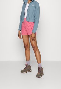 Jasnoniebieska polarowa kurtka na zamek, różowe szorty, szare buty trekkingowe z różowymi akcentami i szare skarpetki. Gładki materiał, casualowy wygląd na świeżym powietrzu.