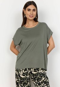 Olivenribbet t-shirt med korte ærmer, rund halsudskæring og løs pasform, parret med mønstrede sort-hvide bukser. Glat tekstur.