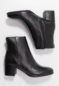 Botas de tobillo de cuero negro con puntera puntiaguda, tacón cuadrado, cremallera lateral y textura suave. Diseño minimalista sin adornos.