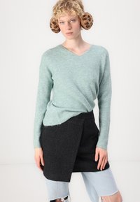 Pullover em malha leve de teal com decote em V, combinado com uma saia preta trapézio. Inclui calções de ganga desgastados em azul claro, criando uma textura em camadas.