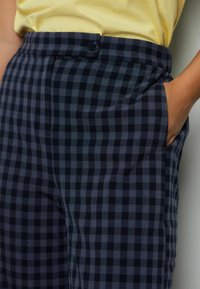 Zwart-grijs geruite broek met een knoopsluiting en zijzakken, met een gladde textuur en een getailleerde pasvorm.