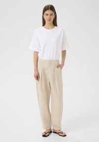 Witte katoenen t-shirt met korte mouwen gecombineerd met hoge, wijde beige linnen broek. Zwarte slippers maken de outfit compleet.
