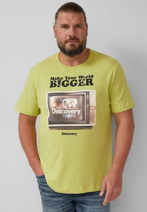 Lichtgele katoenen T-shirt met de tekst "Maak je wereld groter" en een vintage tv-afbeelding met het logo van "The Discovery Channel".