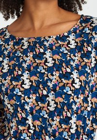 Top con motivo floreale su sfondo blu navy, con accenti blu, bianchi e rosa. Tessuto morbido, scollatura a girocollo e maniche corte.