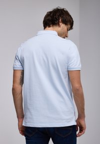 Ljusblå pikétröja med korta ärmar, tillverkad av mjukt bomull. Har en klassisk krage och sidoklyftor vid fållen för ökad rörlighet.