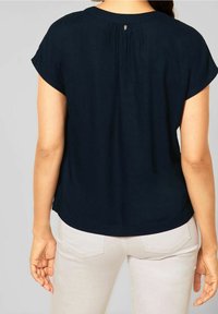 Tummansininen lyhythihainen paita, jossa on pyöreä kaula-aukko, uurrettu selkäosa ja kaareva helma. Kangas näyttää sileältä ja kevyeltä.