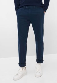 Chinos blu navy, sartoriali, con una texture liscia. Presentano gamba dritta, orli arrotolati e chiusura anteriore con bottone. Abbinati a sneakers bianche.