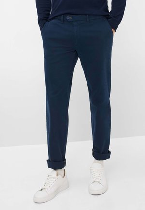 Navy blue, tailored chinos with a smooth texture. Features a straight leg, rolled cuffs, and a front button closure. Paired with white sneakers.