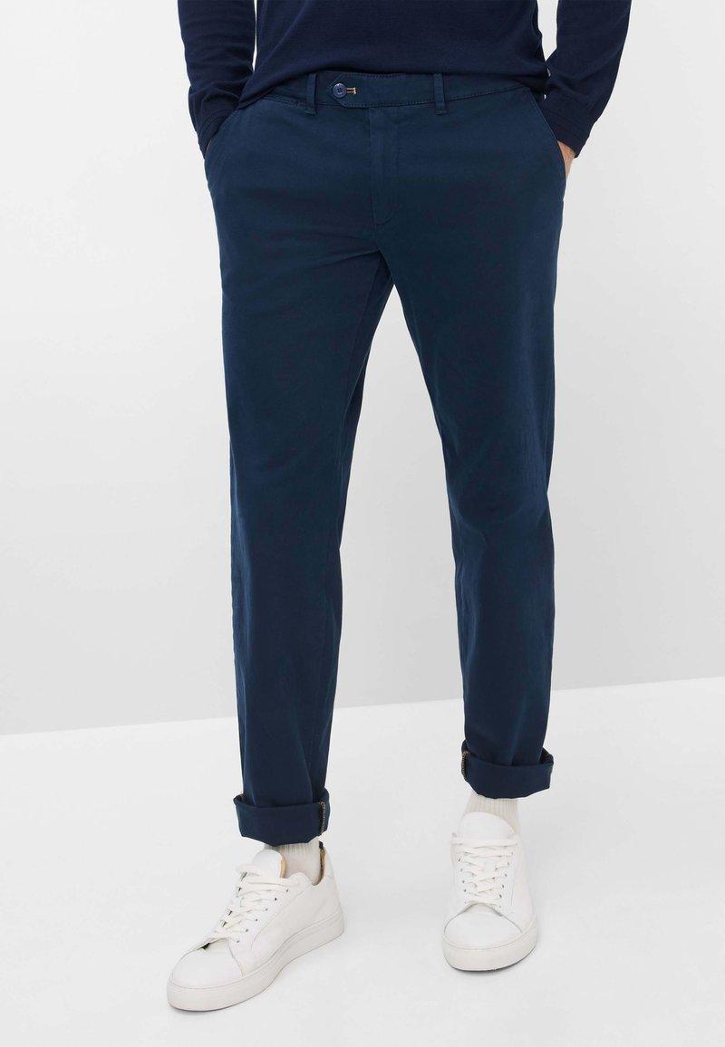 Chinos blu navy, sartoriali, con una texture liscia. Presentano gamba dritta, orli arrotolati e chiusura anteriore con bottone. Abbinati a sneakers bianche.
