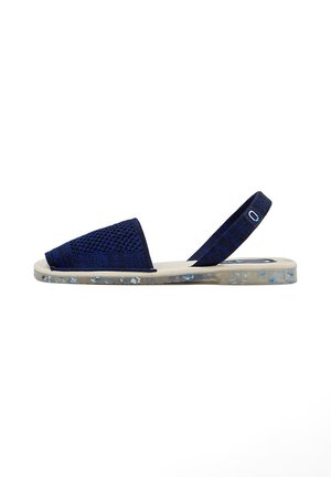 Sandal de tela tejido en azul marino con punta afilada, correa ajustable, suela transparente con destellos de color y diseño plano.