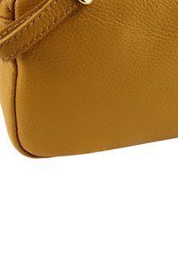 Leren handtas in mosterdgeel met een gestructureerd oppervlak, afgeronde vorm en subtiele stikseldetails langs de randen.