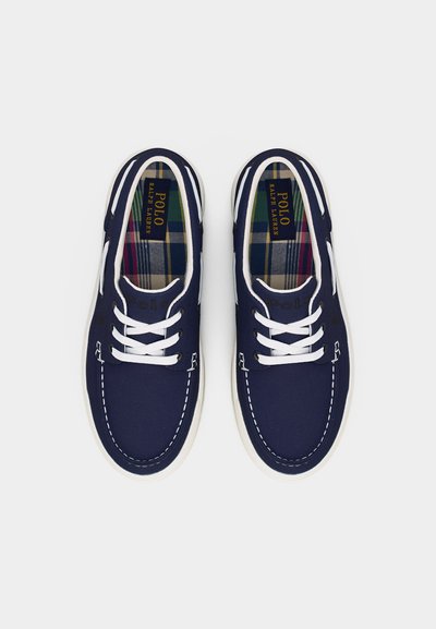 Παντόφλες από καμβά στο χρώμα του ναυτικού μπλε με λευκό ράψιμο, κορδόνια και σόλες, με εσωτερική επένδυση σε καρό σχέδιο και ετικέτες Polo Ralph Lauren στο εσωτερικό.