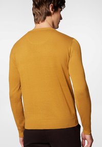 Musztardowy żółty sweter z dzianiny, z długimi rękawami, ribbowymi mankietami i dołem, o gładkiej fakturze i okrągłym dekolcie, widziany z tyłu.