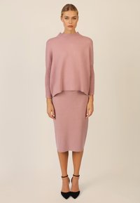 Helles rosa Strickpullover mit hohem Kragen und gerippten Ärmeln, kombiniert mit einem passenden Bleistiftrock und schwarzen Stilettos.