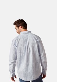 Light blue patterned shirt with a textured surface, buttoned cuffs, and a classic collar, displayed from the back on a model.