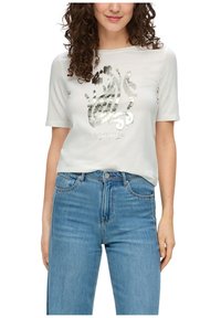 Lichtgrijze t-shirt met korte mouwen en een metallic zilveren grafisch ontwerp en tekst aan de voorkant. Gecombineerd met hoge blauwe jeans.