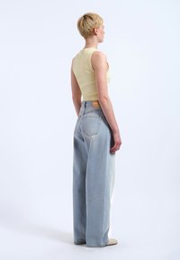 Un haut sans manches jaune clair associé à un jean bleu clair à taille haute et coupe ample, avec une patte en cuir sur le dos et un léger délavage.
