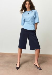 Lyseblå top med korte ærmer, marineblå cropsede bukser med brede ben og sorte spidse hæle med hvide polkaprikker. Enkel design uden mønstre.