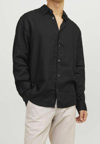 Camicia nera in lino con design a bottoni, maniche lunghe e colletto. Presenta una vestibilità comoda e una trama sottile. I bottoni sono di colore scuro.