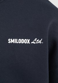 Suéter navy hecho de una mezcla de algodón, con una textura suave y cuello redondo. Logo "SMILODOX Ltd." bordado en blanco en el pecho.