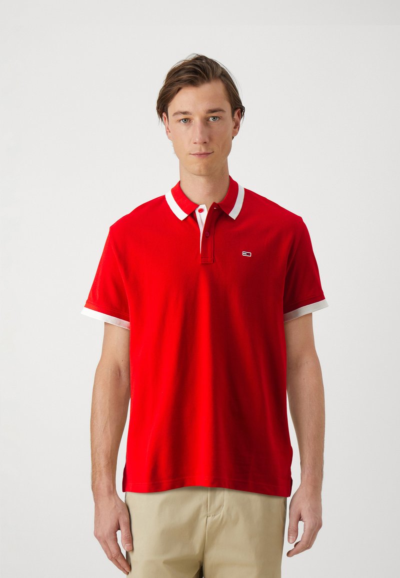 Camisa polo roja con cuello y acentos en las mangas en blanco, con un pequeño logo en el pecho. Confeccionada en una tela suave, de mangas cortas y corte clásico.
