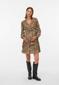 Robe marron avec des motifs de feuilles blanches, décolleté en V, taille cintrée, et manches longues. Portée avec des bottes noires haute jusqu'aux genoux. Tissu lisse.
