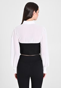 Top corto con maniche lunghe bianche, busto nero e dettagli con bottoni. Abbinato a pantaloni neri a vita alta, con una cintura testurizzata.