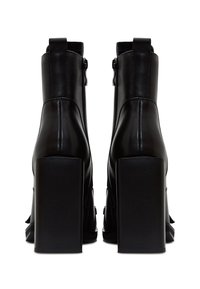 Botines de cuero negro con tacón cuadrado y cierre de cremallera, que presentan una textura suave y un diseño minimalista sin patrones visibles.