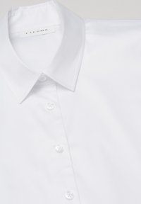 White button-up shirt with a classic collar, featuring a smooth texture and clear plastic buttons. Brand label "ETERNA" visible.