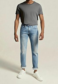 T-shirt gris en coton associé à un jean denim bleu clair, avec une coupe ajustée, des effets usés légers et des revers retroussés. Des baskets blanches complètent le look.